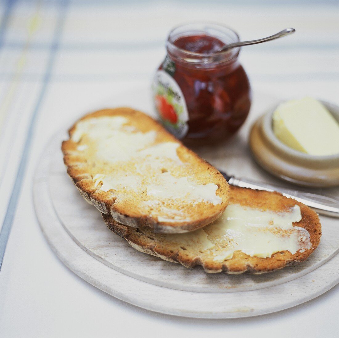 Getoastetes Brot mit Butter, dahinter Marmeladenglas