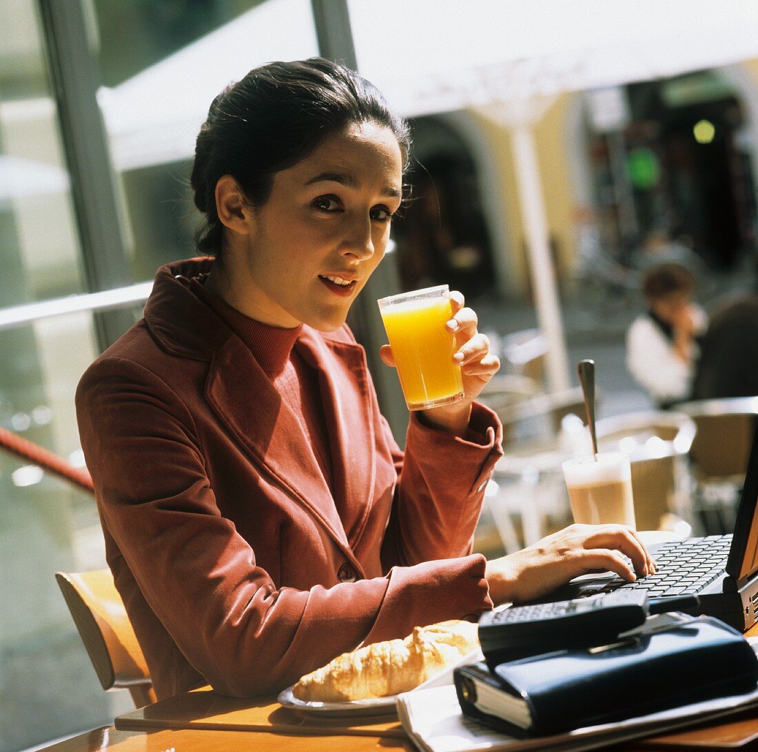 Geschäftsfrau sitzt mit Orangensaft im Café vor Laptop