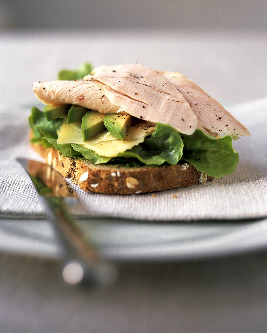 Belegtes Brot mit Truthahnbrust, Avocado, Käse uns Salatblatt