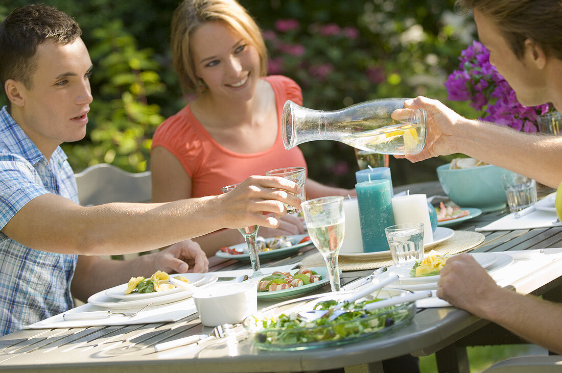 Junge Leute mit Vorspeisen und Wasser am Tisch im Freien