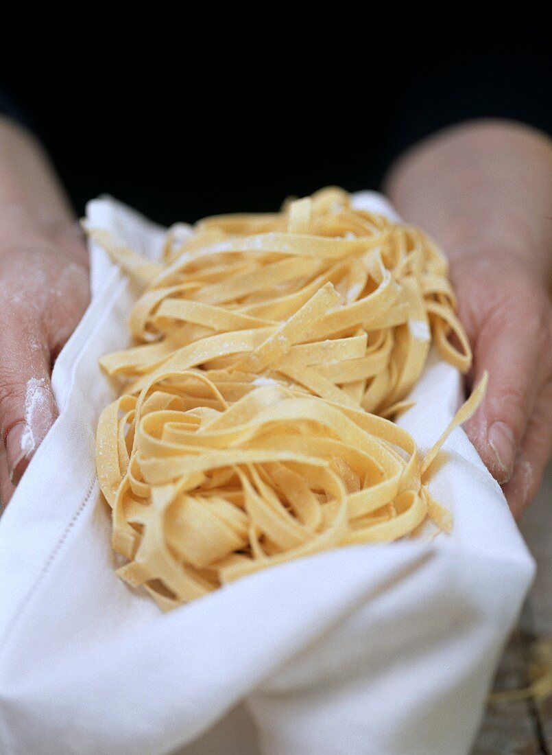 Hands holding home-made ribbon pasta on tea towel