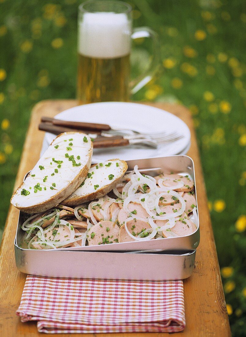 Sausage salad with onions in picnic box; bread & butter; beer