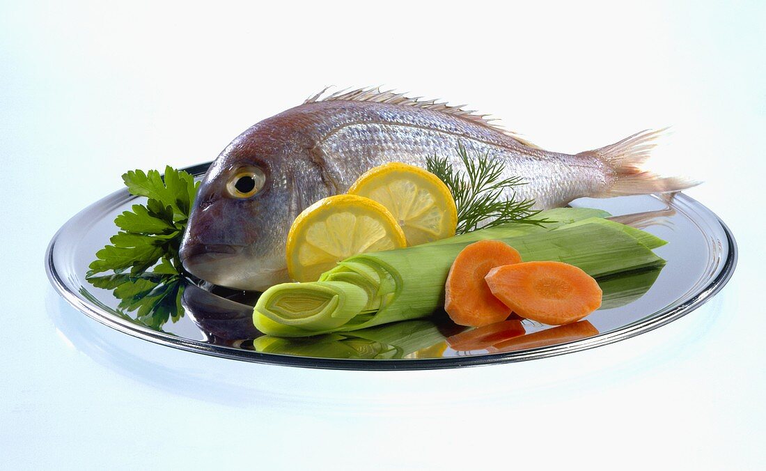 Fresh gilthead bream, garnished with vegetables and lemon
