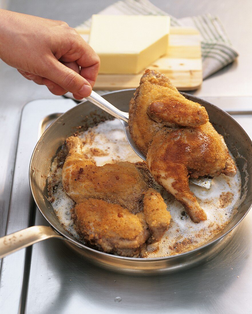 Taking fried breaded poussin out of the frying pan