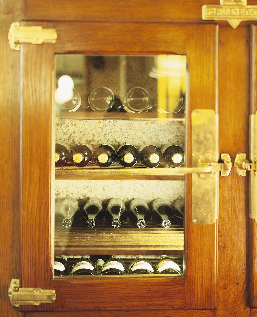 Mehrere Weinflaschen in holzverkleidetem Barfach mit Fenster