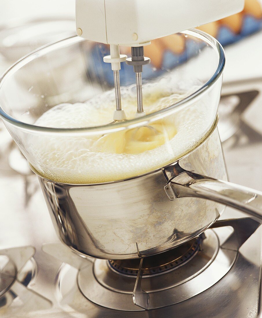 Mixing egg yolks with sugar in bowl over bain-marie