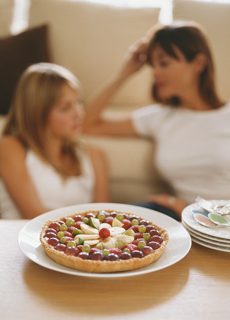 Fruit cake on table, woman and girl on sofa behind