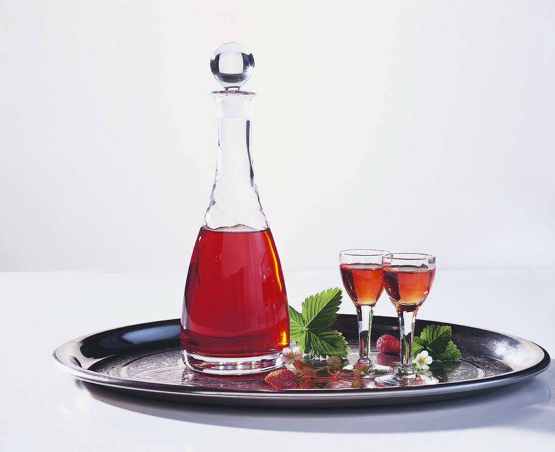 Wild strawberry liqueur in carafe and glasses on tray