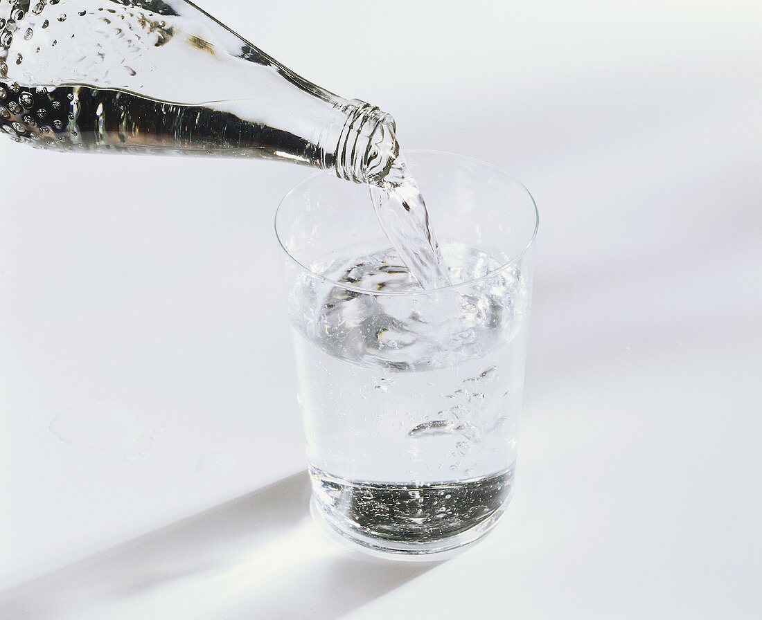 Mineralwasser aus Flasche in Glas einschenken