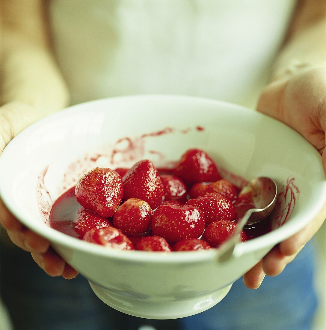 Person hält Schüssel Erdbeeren mit Fruchtsauce
