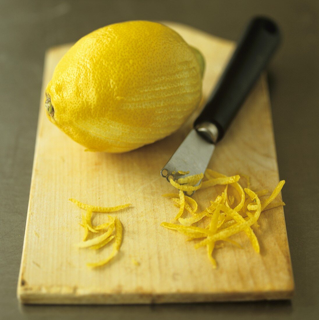Zitrone, Zitronenzesten und Zestenreisser auf Schneidebrett