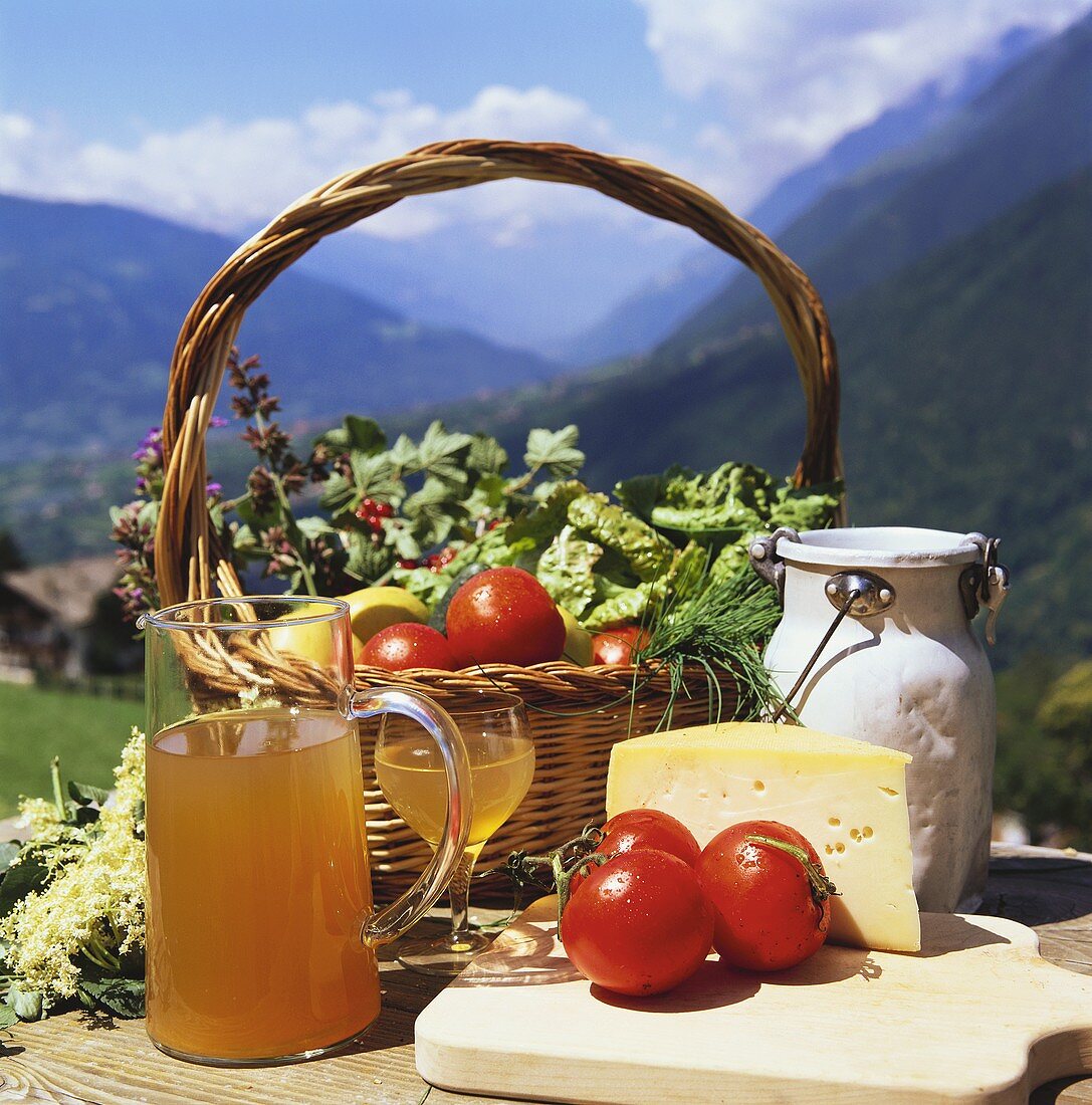 Korb mit Gemüse, Milchkanne, Käse und Apfelsaft auf Holztisch