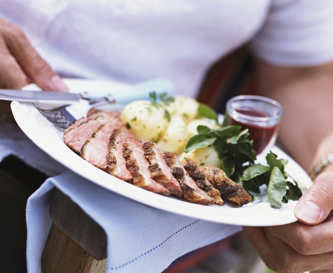 Person holding plate of roast beef and parsley potatoes