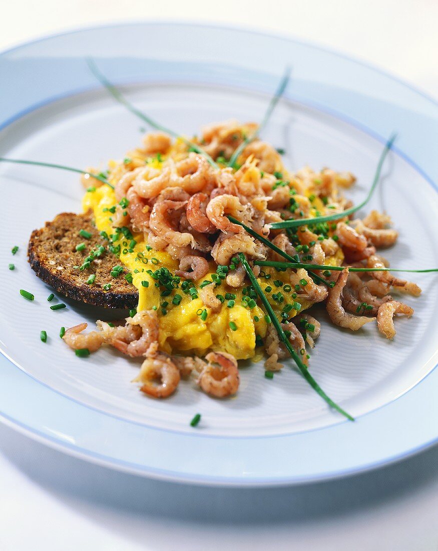 Scrambled egg with shrimps and chives on black bread