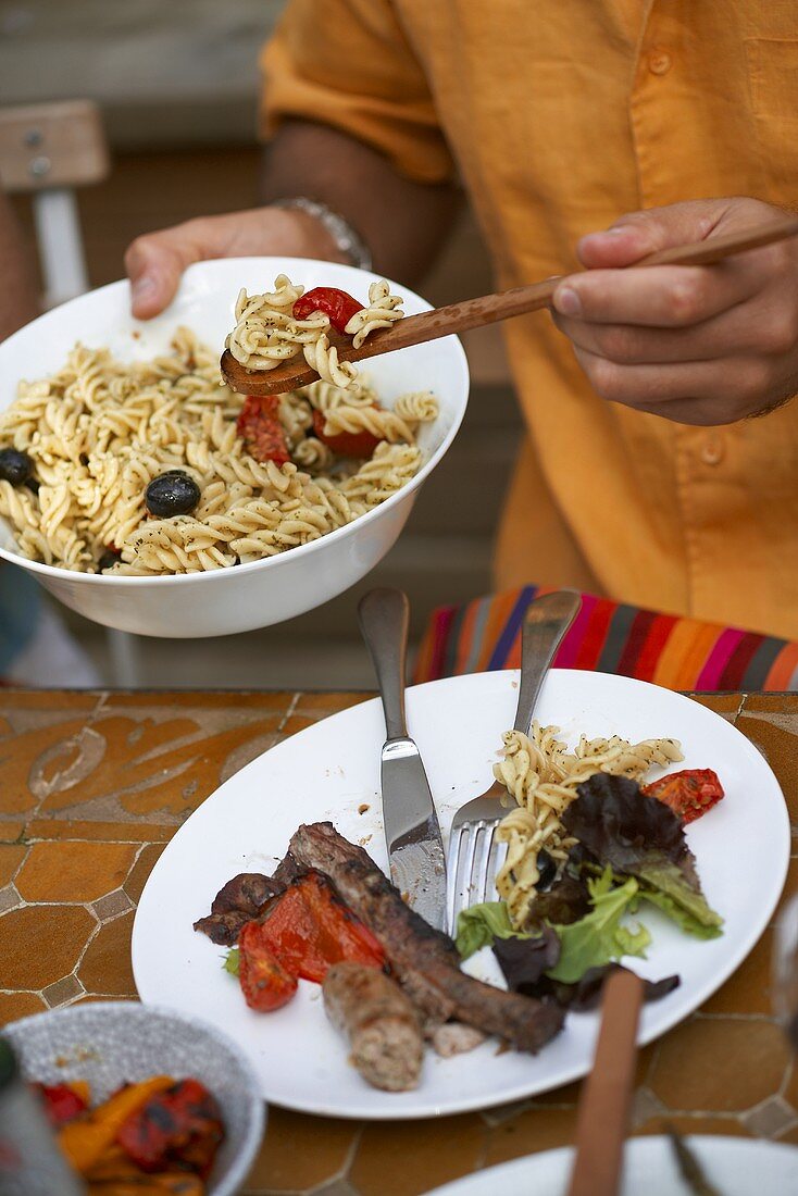 Man putting pasta salad on plate of barbecued food