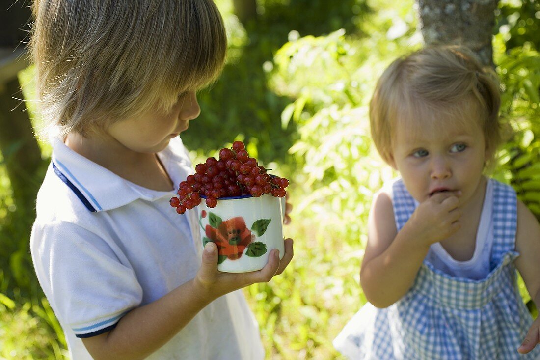 Mädchen und Junge mit roten Johannisbeeren im Freien