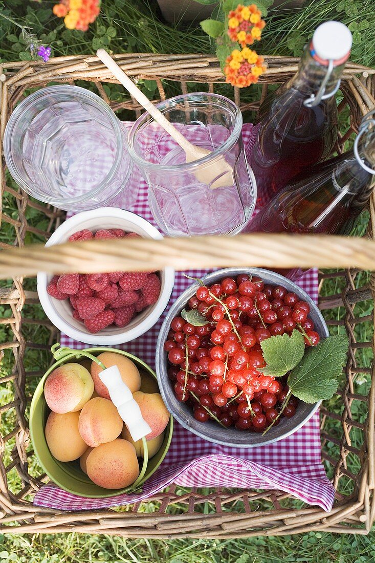 Berries, apricots, bottles of juice and jars in basket