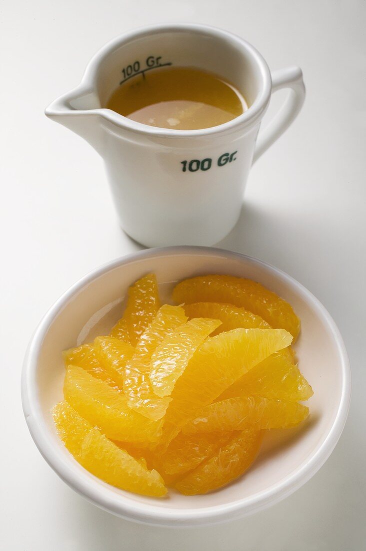 Orange segments in white bowl, orange juice in measuring jug