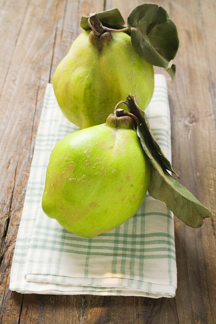 Two quinces with leaves on tea towel