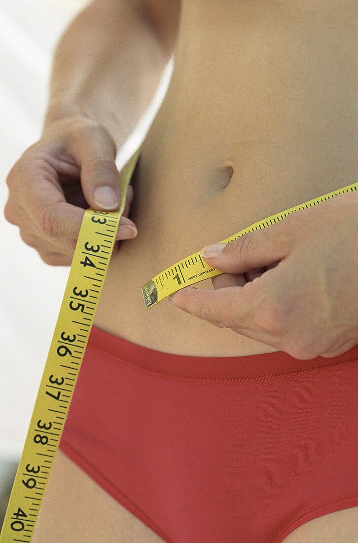 Person measuring their waist with tape measure