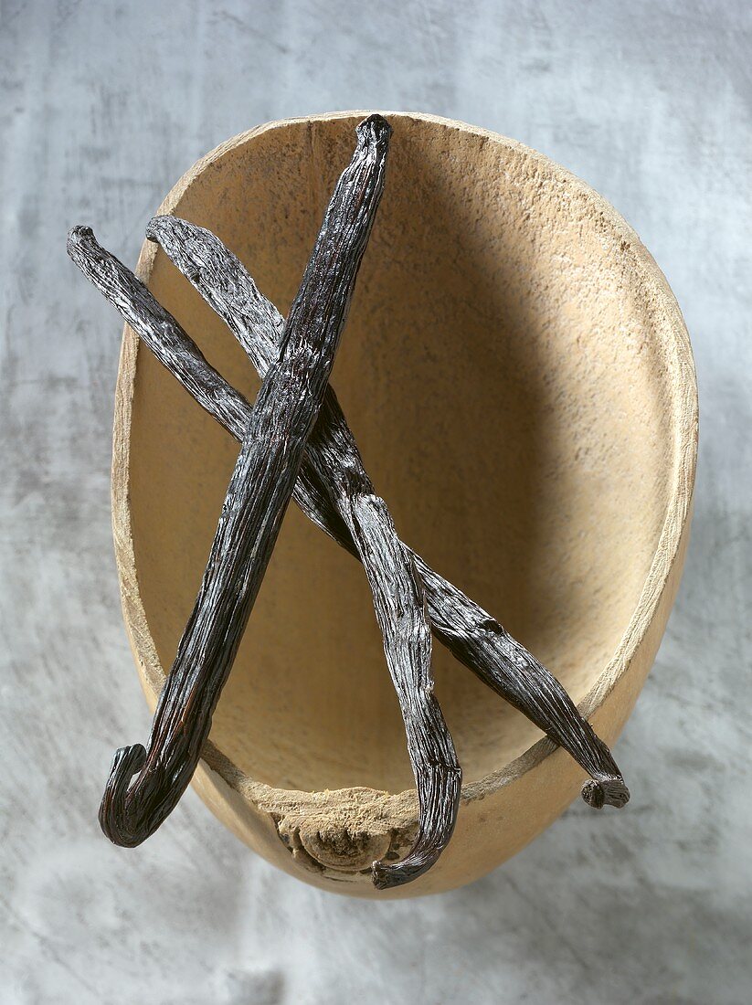 Three vanilla pods laid across wooden bowl