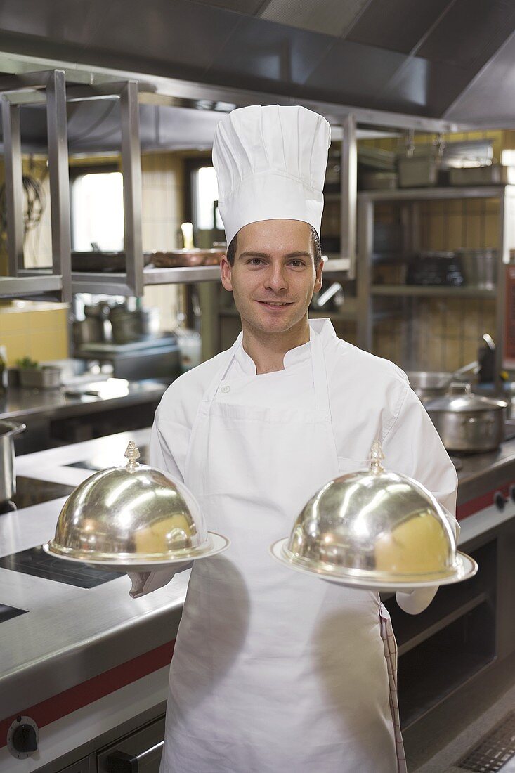 Chef with two domed serving platters in his hands