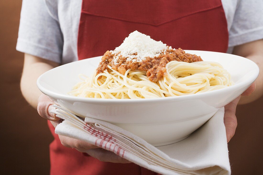 Person serviert Spaghetti Bolognese mit Parmesan