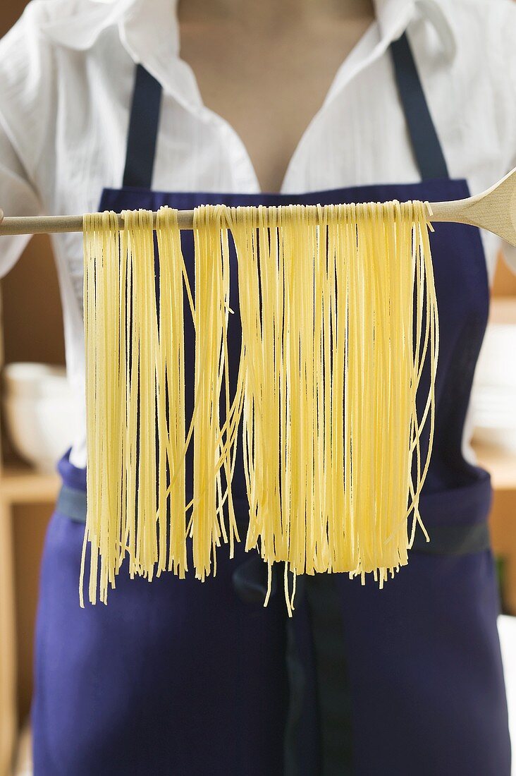 Hanging home-made pasta over wooden spoon to dry