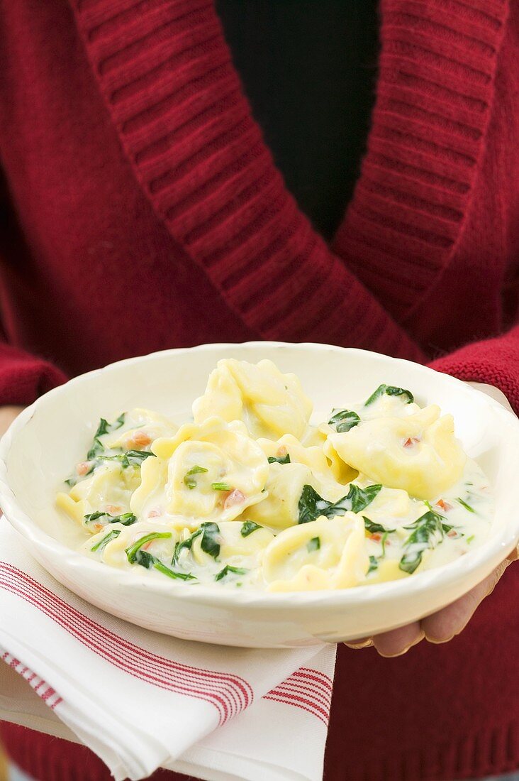 Frau hält Teller Tortellini mit Spinat und Sahnesauce