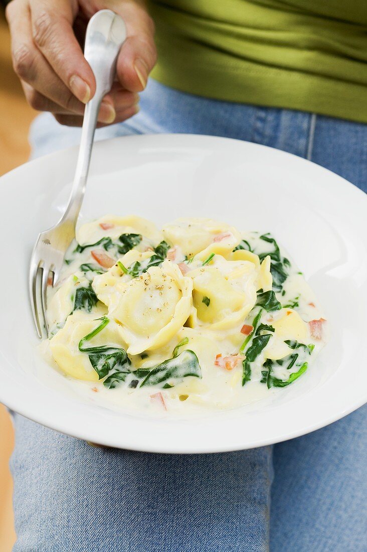 Person isst Tortellini mit Spinat und Sahnesauce