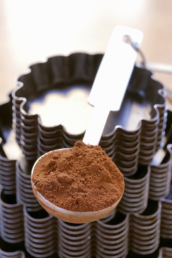 Ein Löffel Kakaopulver auf gestapelten Backformen