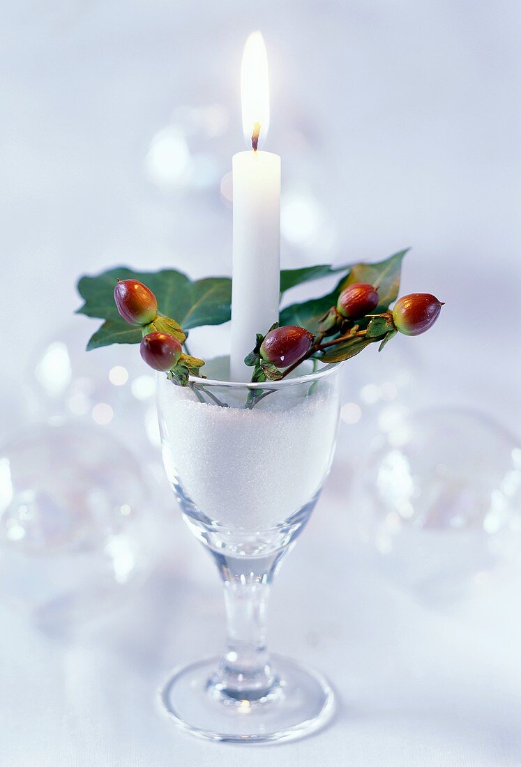 Festive table decoration with candle & rose hips in wine glass