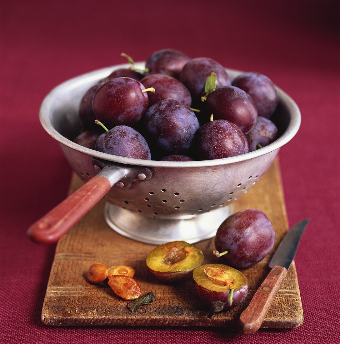 Fresh plums in and beside a colander on a chopping board