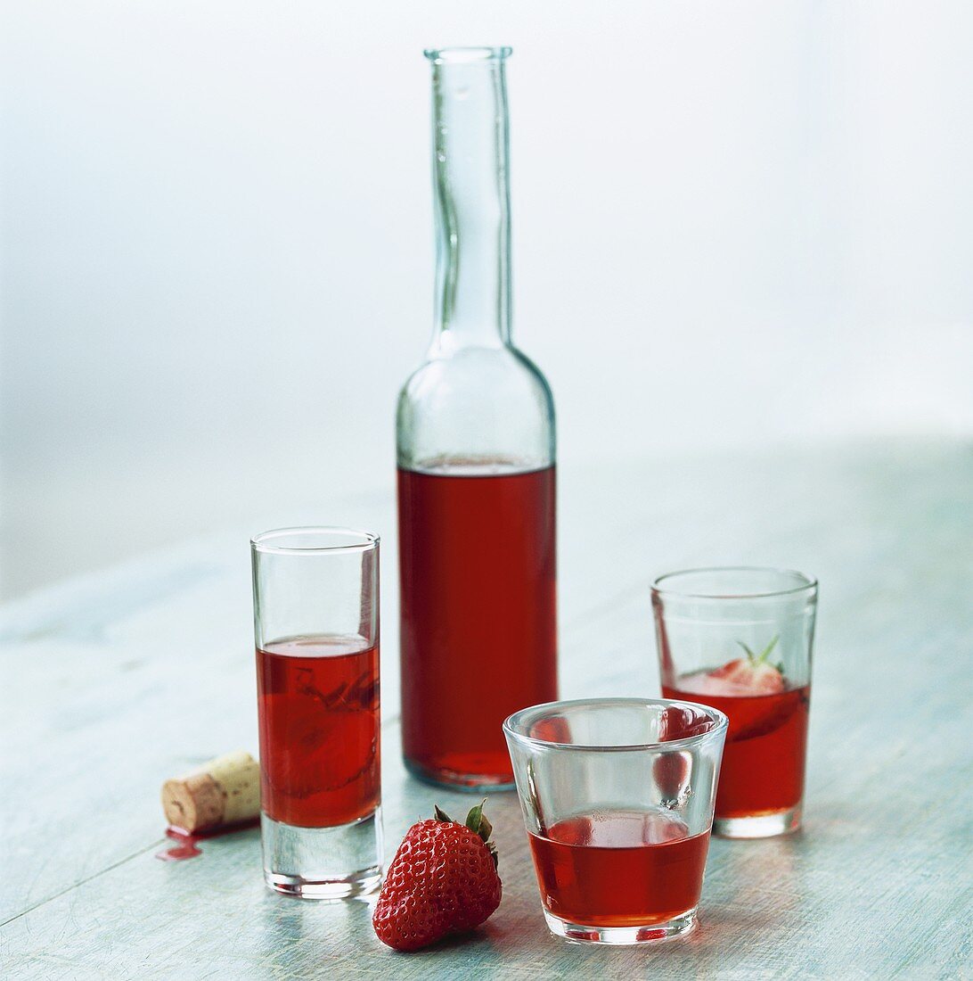 Erdbeerlikör in Flasche und drei verschiedenen Gläsern