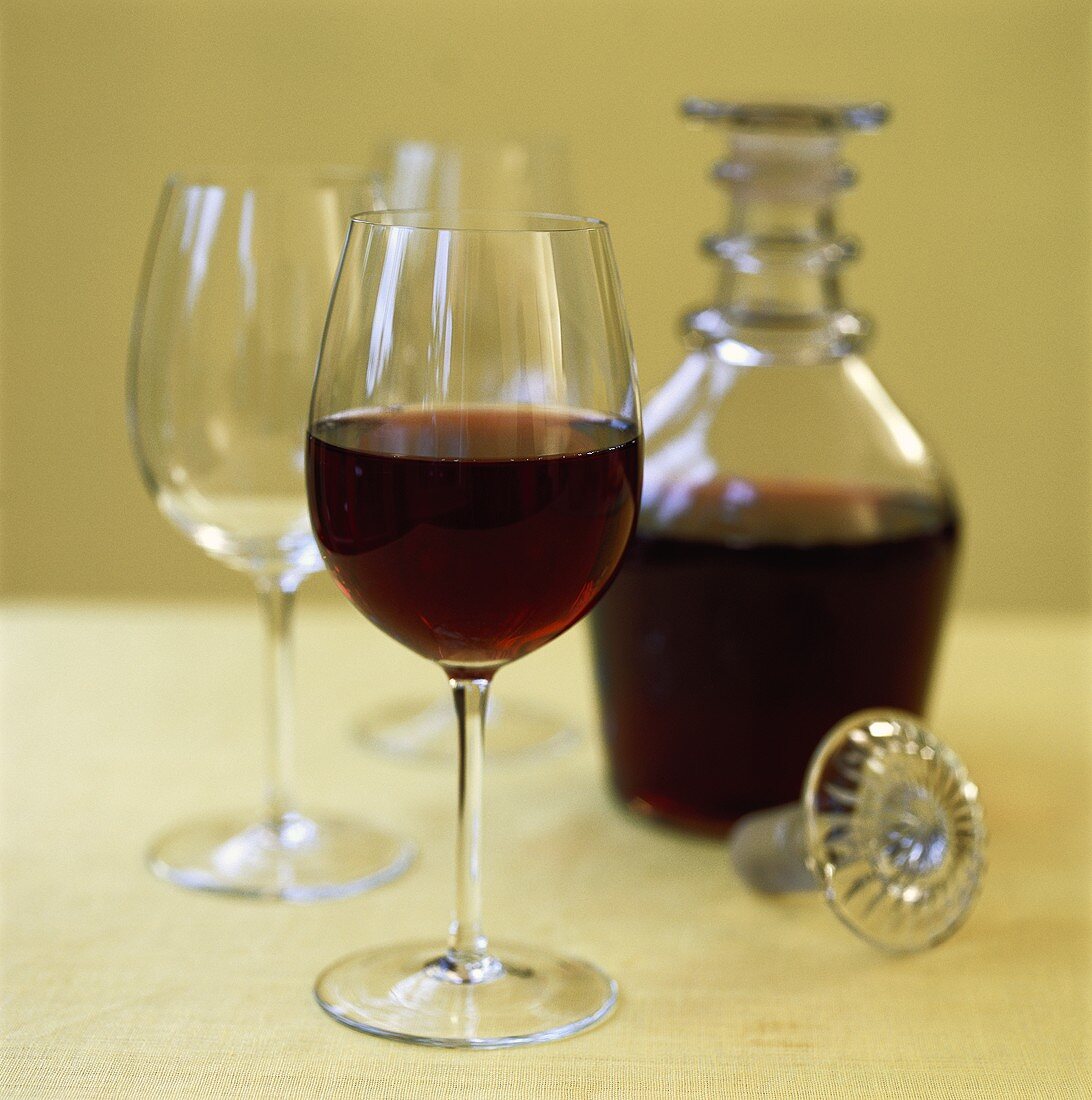 Red wine in glass and carafe beside empty wine glasses