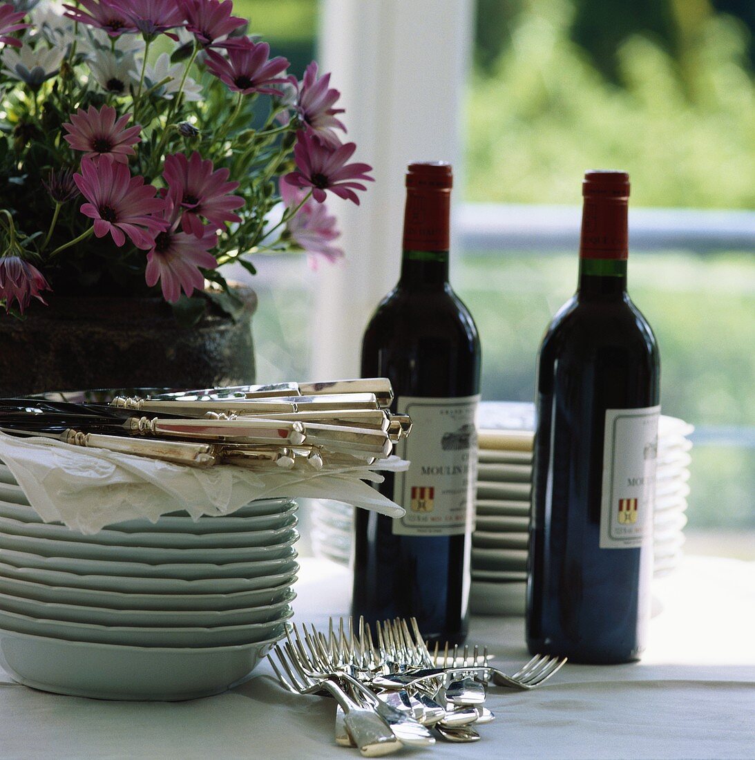 Tellerstapel, Besteck, Rotwein und Blumen auf Tisch