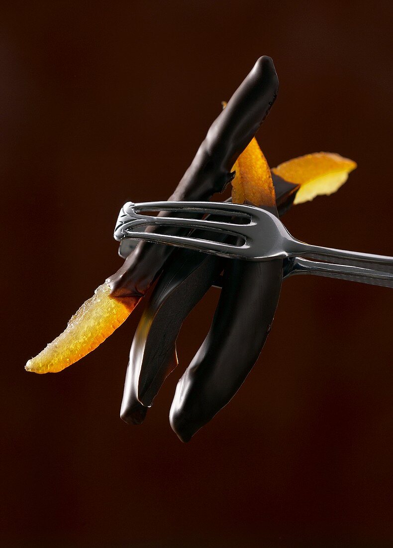 Chocolate-coated candied orange held in tongs