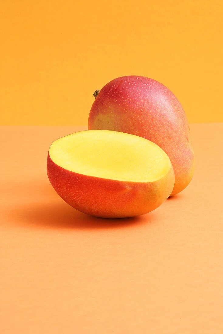 Ganze und halbe Mango auf farbigem Hintergrund