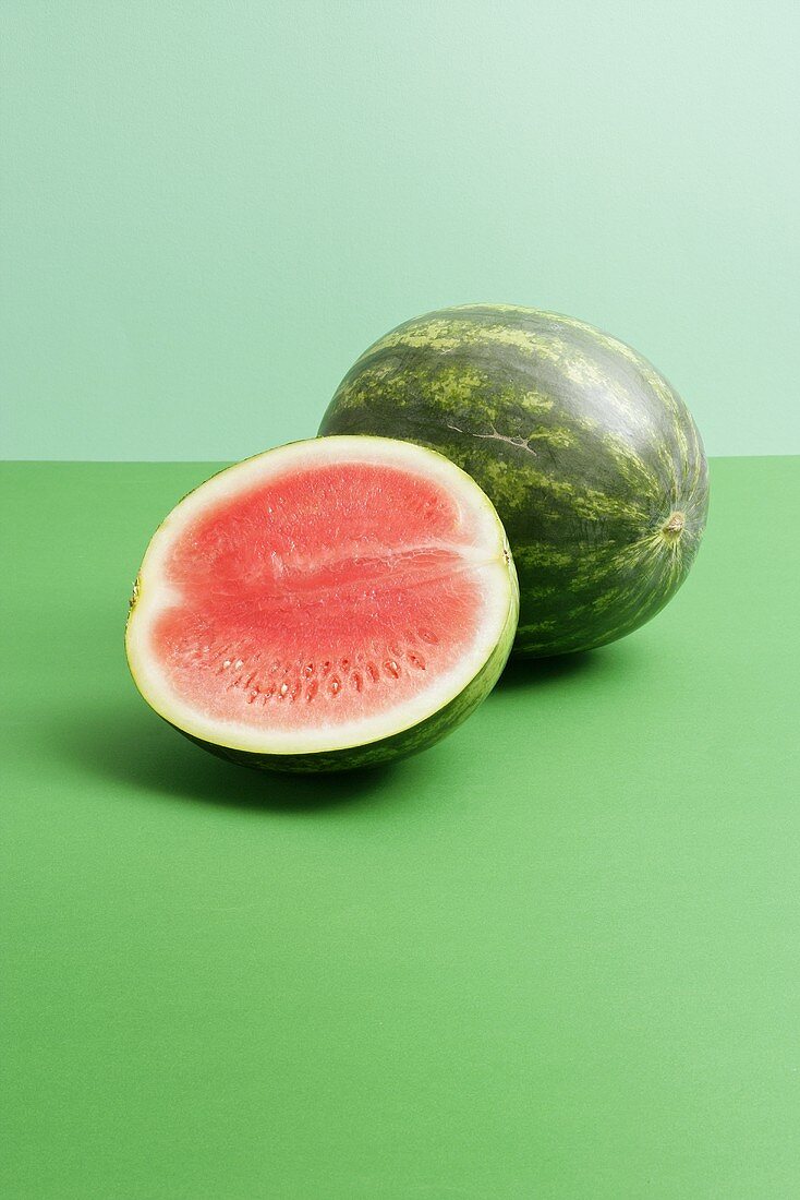 Ganze und halbe Wassermelone auf grünem Hintergrund