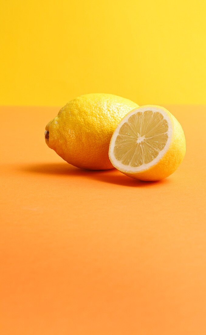 Ganze und halbe Zitrone auf farbigem Hintergrund