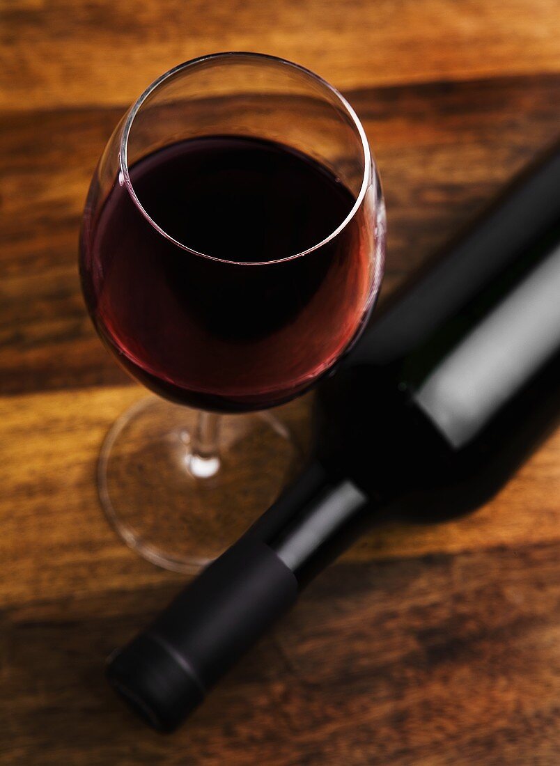 Glass of red wine beside red wine bottle on wooden surface