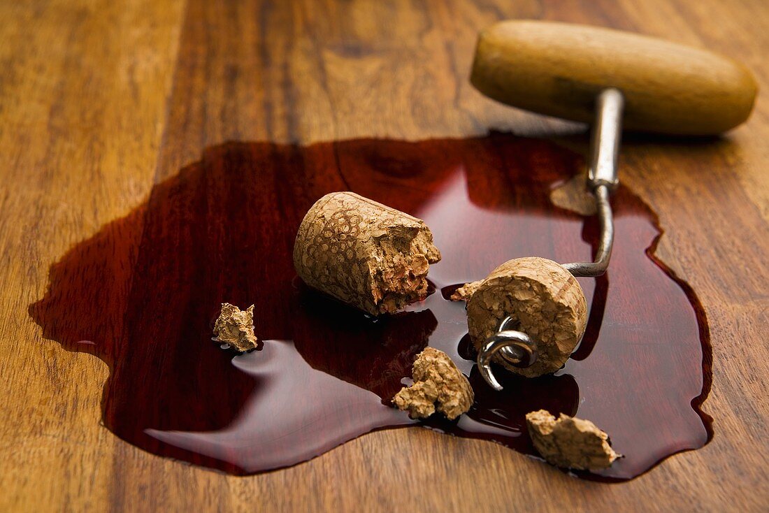 Corkscrew and broken cork in pool of spilt red wine