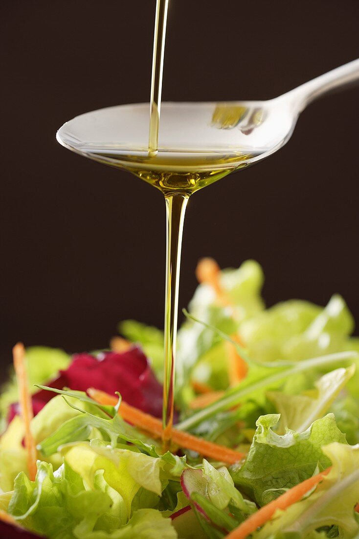 Olivenöl fliesst über Löffel auf gemischten Blattsalat