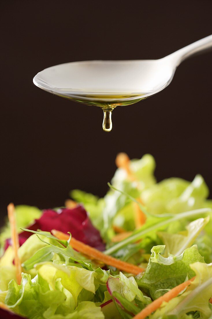 Olivenöl tropft vom Löffel auf gemischten Blattsalat