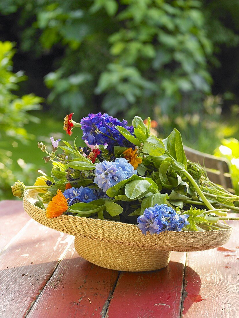 Summer flowers in a straw hat on a garden table