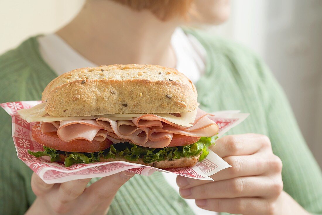 Frau hält Schinken-Käse-Sandwich auf Papierserviette