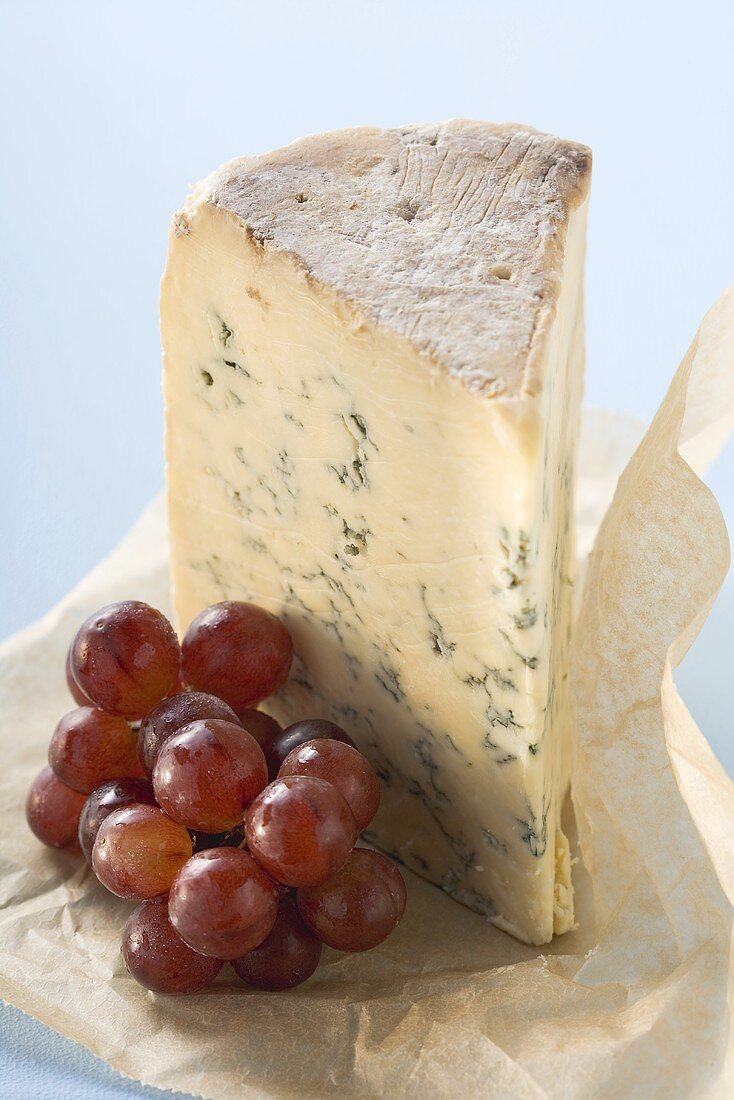 Piece of Stilton and red grapes on paper