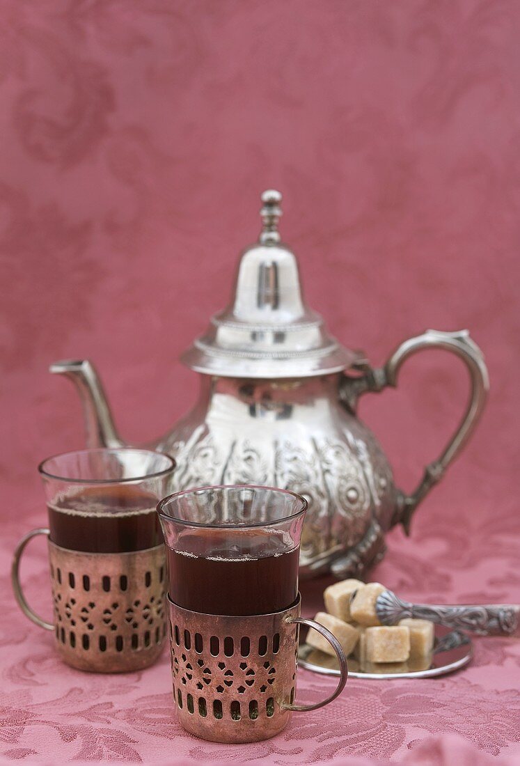 Two glasses of black tea, sugar cubes, silver teapot
