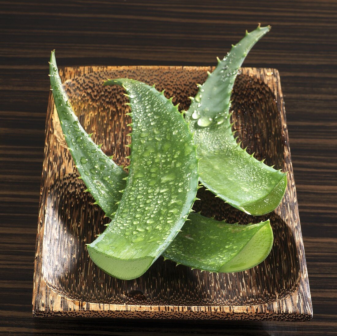 Aloe vera leaves with drops of water in wooden dish