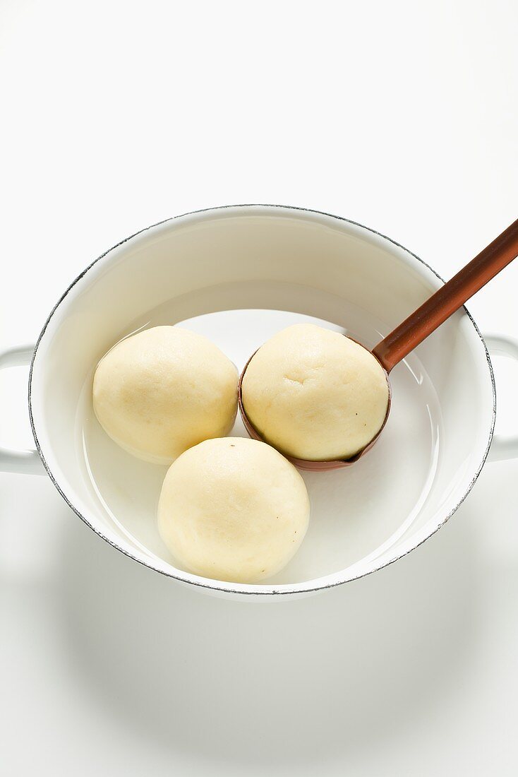 Three potato dumplings in water with ladle